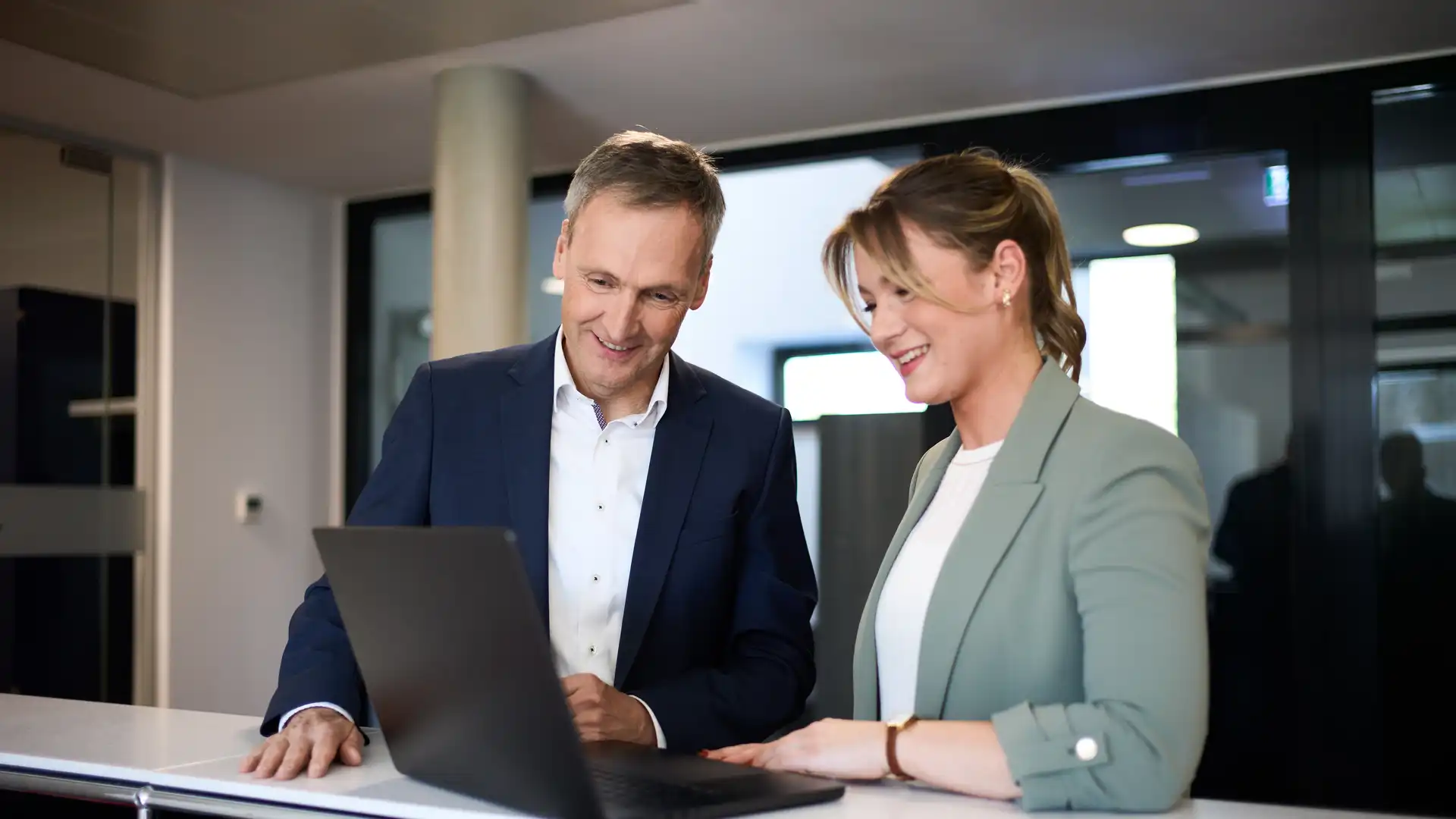 Eine Frau und ein Mann stehen an einem Tisch und schauen auf ein Laptop