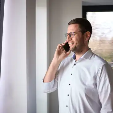 Ein Mitarbeiter, der vor einem Fenster steht und telefoniert.